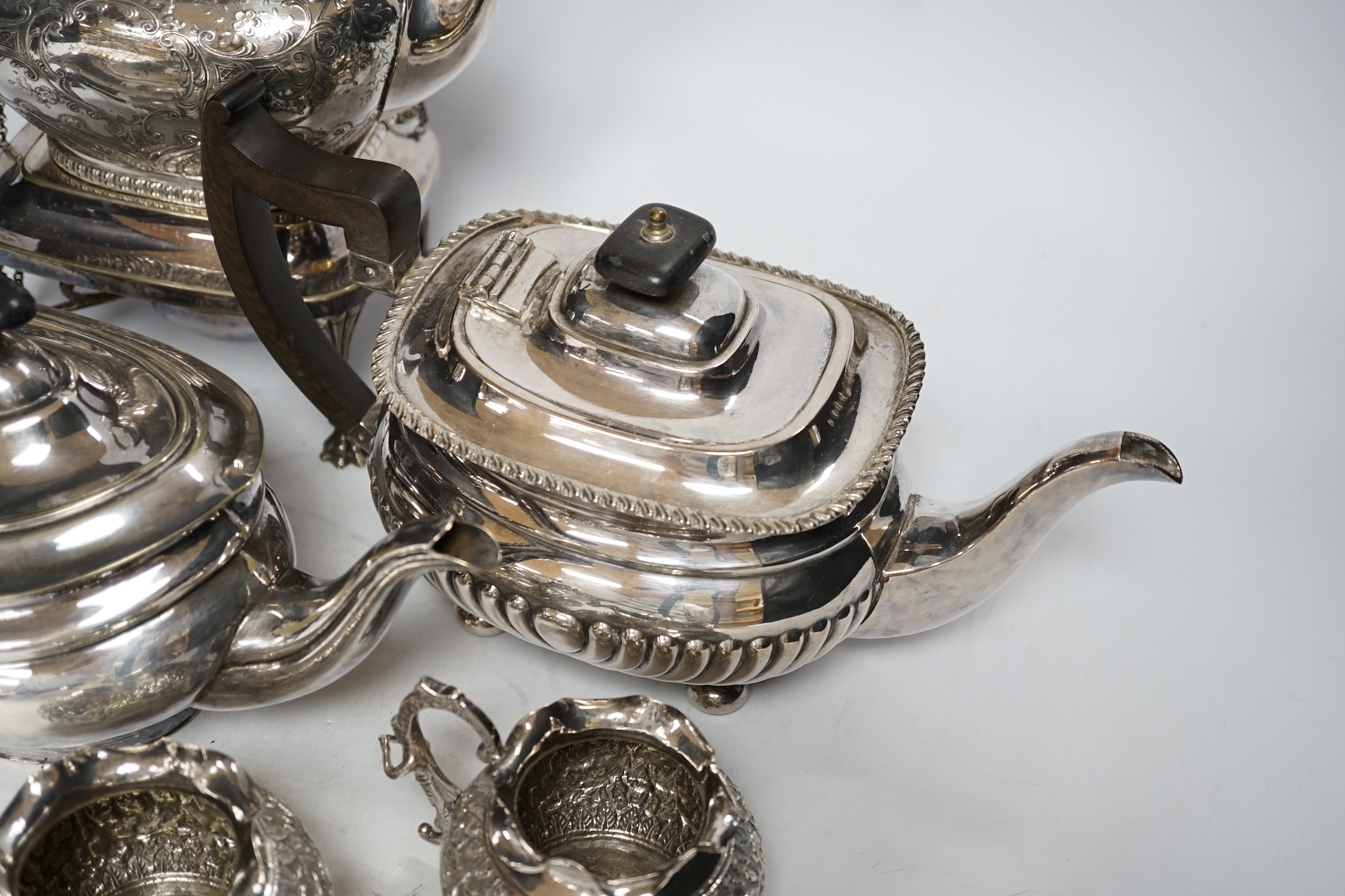 A plated kettle on stand, two plated teapots, a sugar bowl and a cream jug